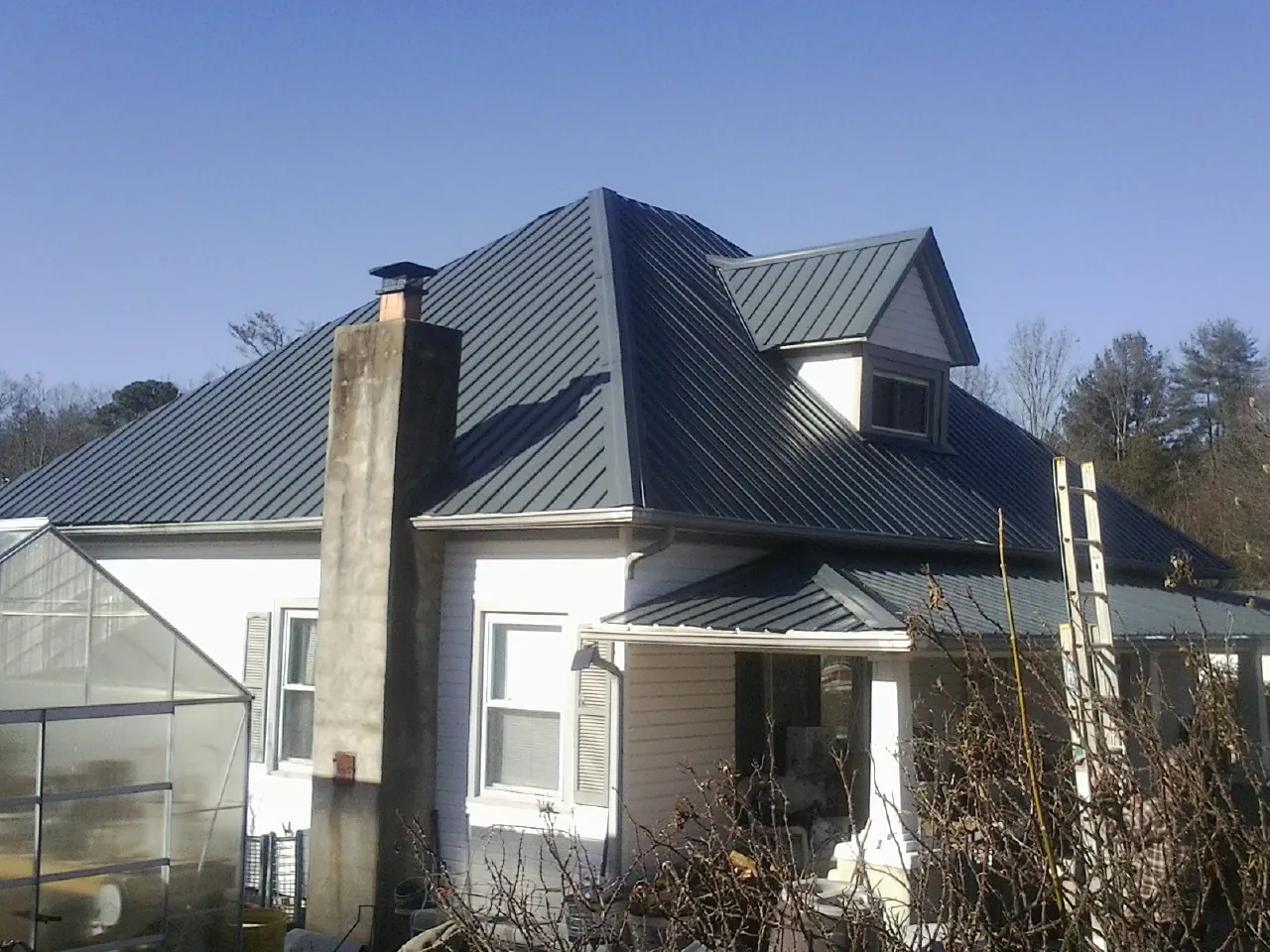 Dark blue standing seam metal roof on a white farmhouse with dormer — Slate & Tile Roof Repair by Roofing Brothers in Corrigan