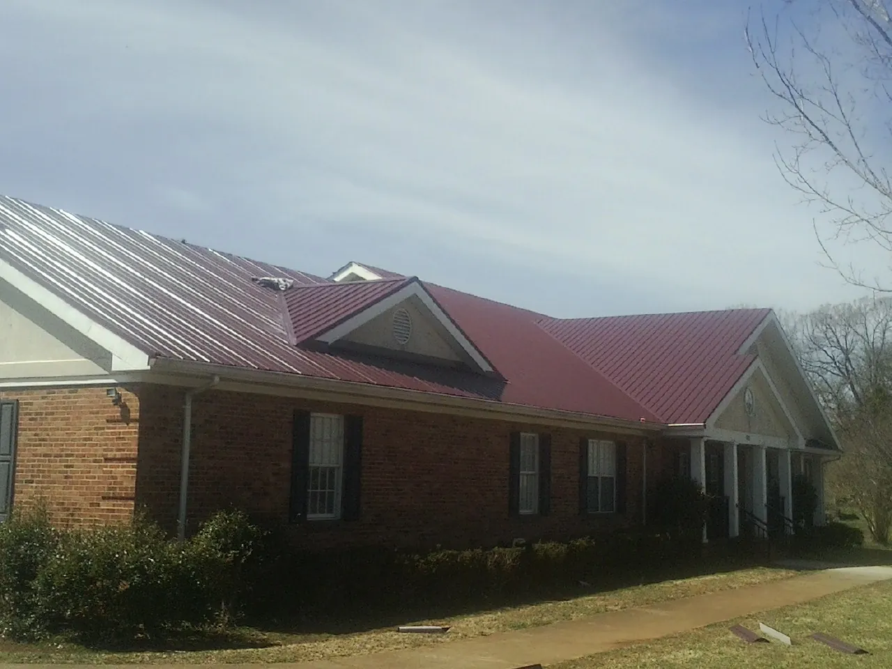 Red metal roof with gabled entries on a long brick building, from a Hail Damage Roof Repair job in Corrigan
