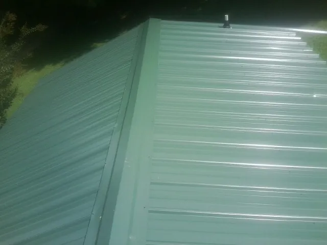 New green metal panels meeting at the ridge of a roof — Flat Roof Repair work by our crew in Corrigan