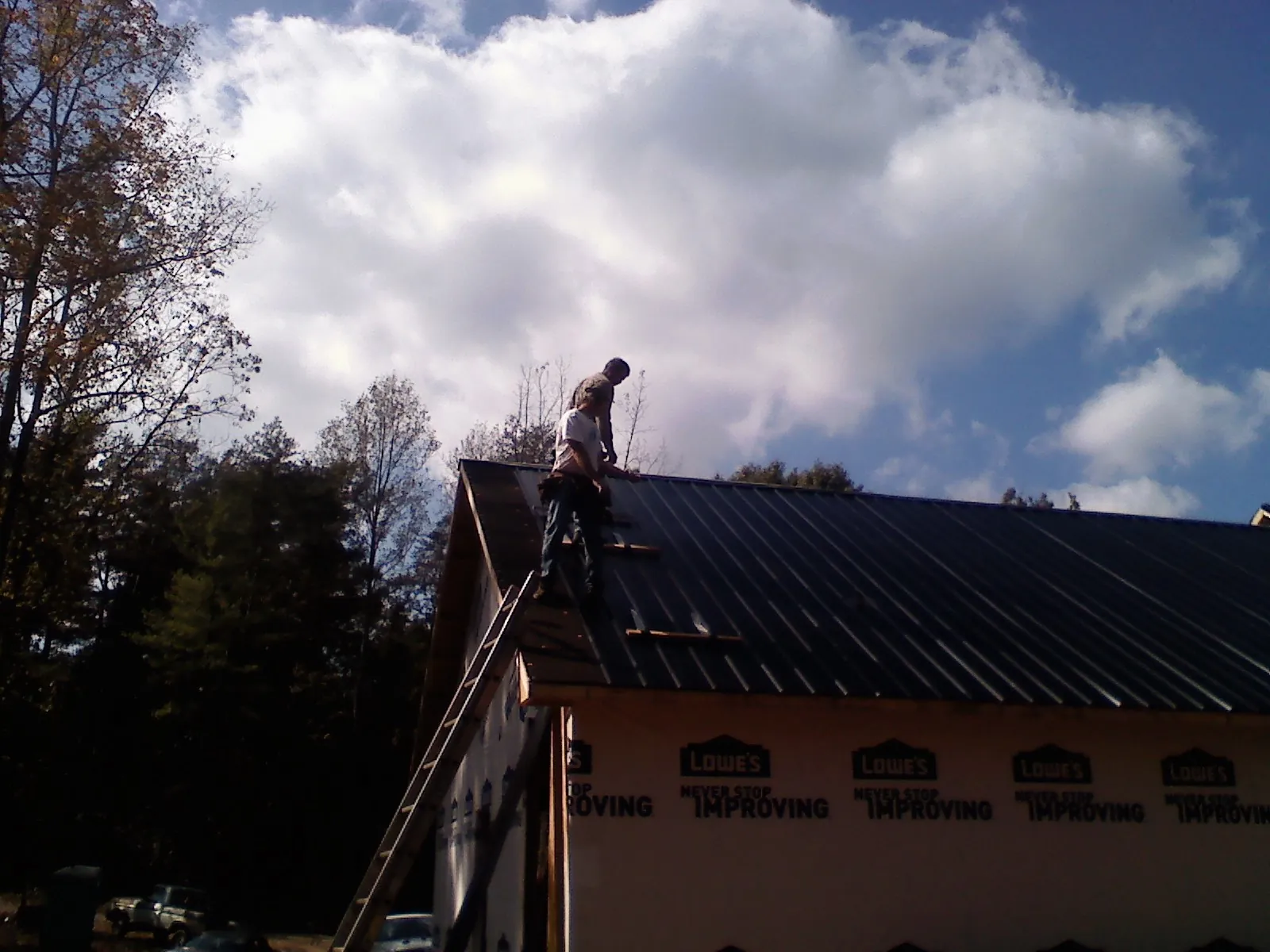 Roofer fastening dark metal panels high against a cloudy sky, from a Roof Inspection job in Corrigan