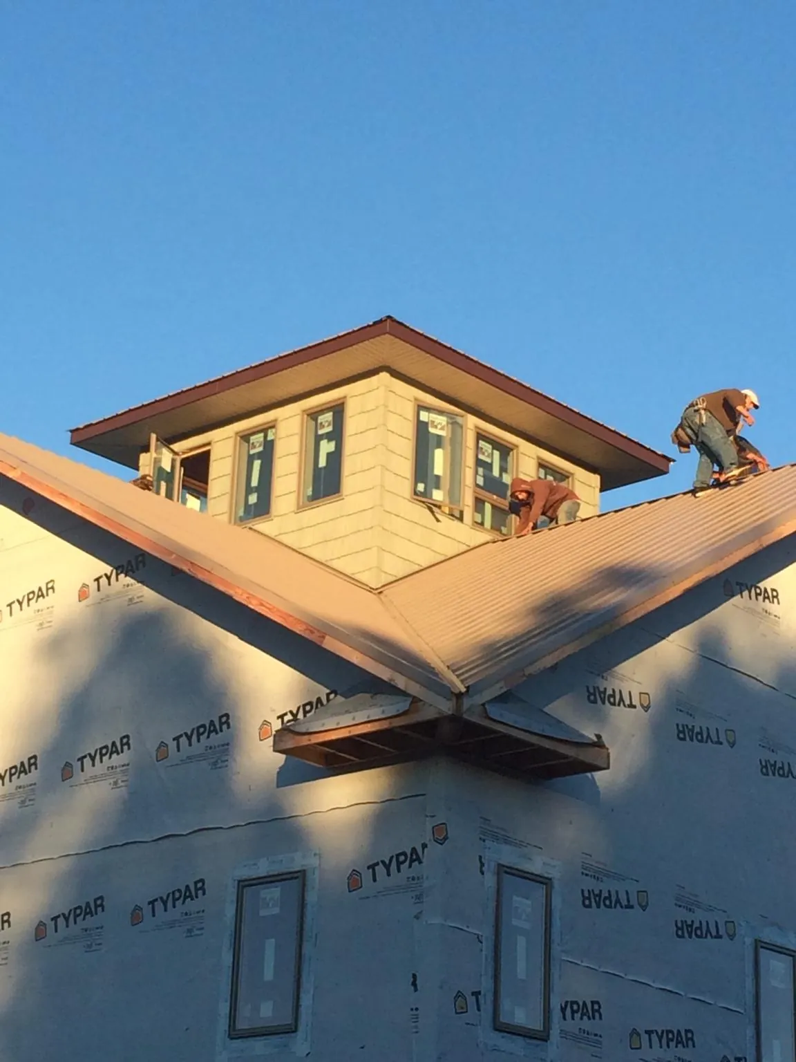Roofers working around a rooftop cupola on a new metal roof at sunset — Roof Waterproofing in Corrigan by Roofing Brothers